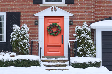 Front door of snow covered house with Christmas wreath