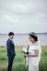 Smiling bride holds a wedding bouquet in her hands and the groom is wearing a suit on background the green meadow.