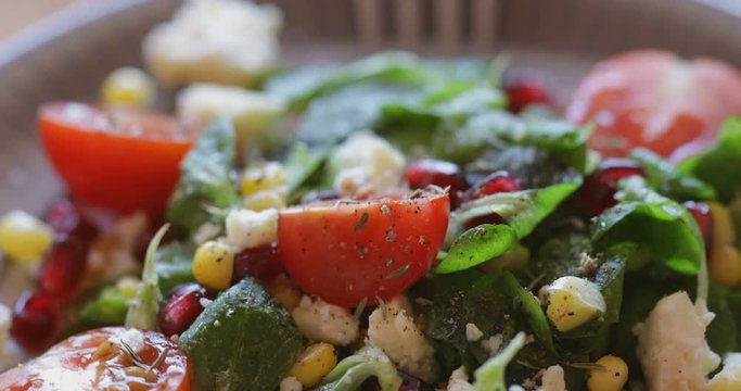 Fresh made corn salad with cherry tomatoes, soft cheese, sweetcorn kernel and pomegranate seed on plate on rotating stand, close up