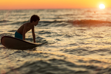 silhouette of a child with a surfboard in the defocus in the evening hours