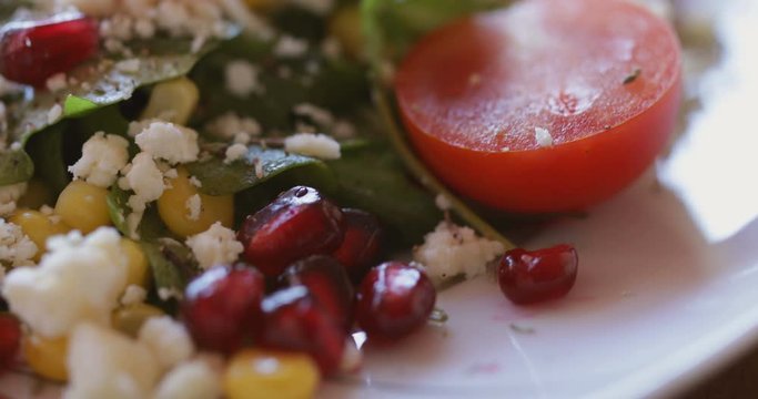 Fresh made arugula salad with cherry tomatoes, soft cheese, sweetcorn kernel and pomegranate seed on plate on rotating stand, close up