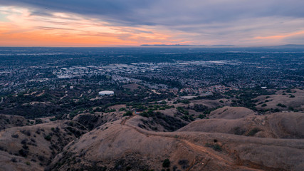 Aerial view of open rolling hills in suburban Southern California.  Radio tower atop hill during sunset surrounded by mountains and ocean
