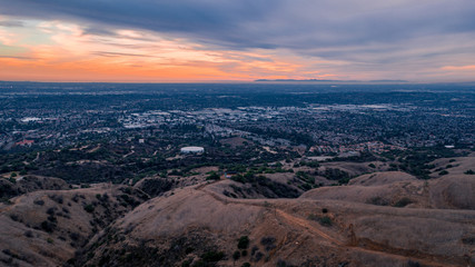 Fototapeta na wymiar Aerial view of open rolling hills in suburban Southern California. Radio tower atop hill during sunset surrounded by mountains and ocean