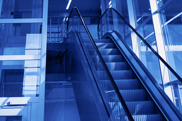 New and modern escalator moving up. Building of international airport or railway station. Toned in classic blue color, blurred and selective focus. Fashionable color of the New Year 2020.