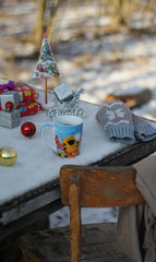 Table in the forest in winter. On the table is a mug of tea and Christmas toys.