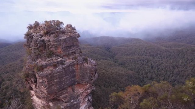 Slow panorama aerial view of the Three Sisters rock formation in the Blue Mountains, while a bushfire burns in the Jamison Valley below creating an ethereal curtain of misty smoke