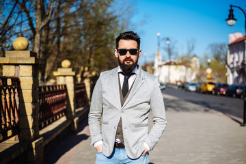 Young successful handsome man in a gray jacket is standing on the street