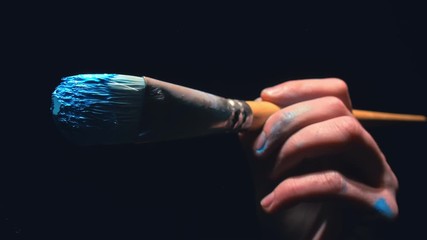 The artist draw on glass. Back view. Craftsman decorator use large brush and blue acrylic oil paint. Indoor. Dark magic cinematic look, black background. Artist Brush draw directly on glass screen. - Powered by Adobe