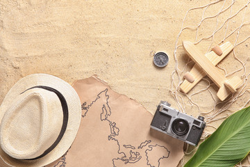 Map with photo camera, wooden airplane, compass and hat on sand