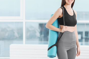 Sporty young woman with yoga mat in gym