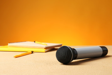 Microphone and notebooks on table against color background