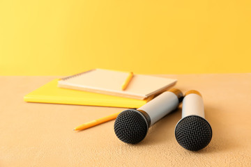 Microphones and notebooks on table against color background