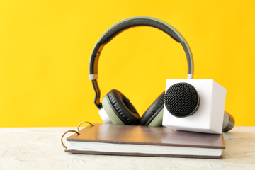 Microphone, headphones and notebook on table against color background - obrazy, fototapety, plakaty