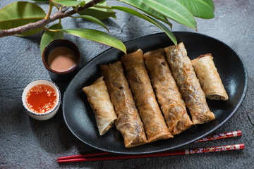Black plate with vietnamese nems or deep fried spring rolls and dipping sauces over grey stone...