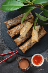 Top view of vietnamese fried spring rolls or nems on a stone slate tray with dips, vertical shot