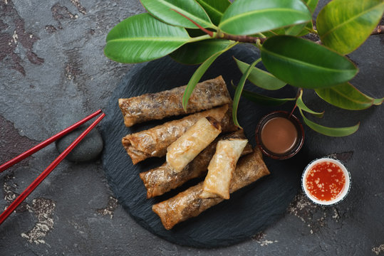 Stone slate tray with nems or vietnamese deep fried spring rolls, top view over brown stone background with a ficus tree