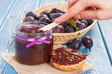 Hand with knife preparing fresh sandwiches with plum marmalade or jam, healthy sweet breakfast concept
