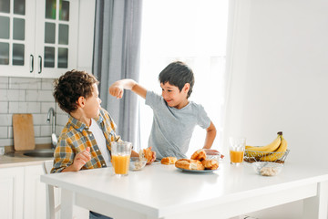 Two siblings tween boys real brothers fight at breakfast table on bright kitchen at home
