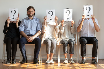 Confident young man sitting on chair in queue of unknown people.