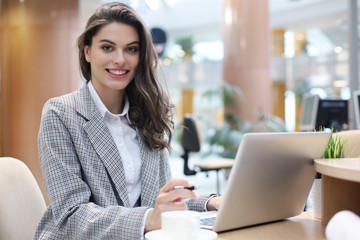 Portrait of a cheerful young businesswoman sitting at the table in office and looking at camera.