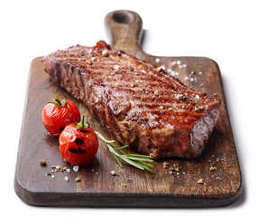 Grilled beef steak on wooden board isolated on white background with tomatoes and rosemary