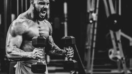 Brutal athletic bodybuilder training with heavy dumbbells in modern fitness club, dramatic black and white image - Powered by Adobe