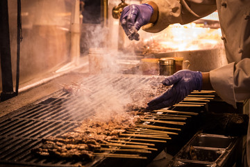 Close up of preparing grill beef on BBQ grill. Meat skewers ( Chinese street food) are cooked by chef at Night Market. Beef skewers grilled over charcoal visible fire and smoke .