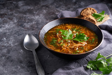 Traditional European and Russian soup borsch with cabbage and meat served in a plate on a dark stone table.