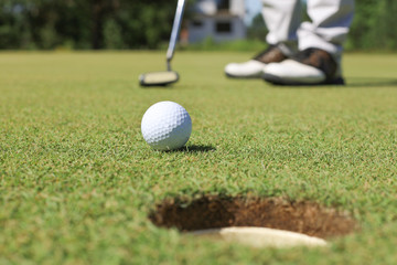 Golf player at the putting green hitting ball into a hole.