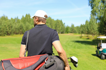 Golf player walking and carrying bag on course during summer game golfing.