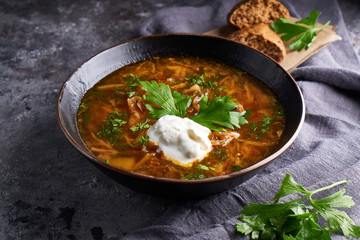 Traditional European and Russian soup borsch with cabbage, sour cream and meat served in a plate on a dark stone table.
