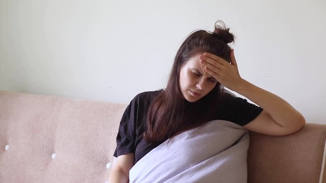 Sick young woman sitting at home with severe headache	