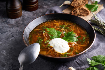 Traditional European and Russian soup borsch with cabbage, sour cream and meat served in a plate on a dark stone table