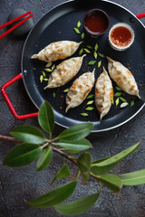 Serving pan with fried potstickers dumplings and dipping sauces, top view over grey stone surface with a ficus tree
