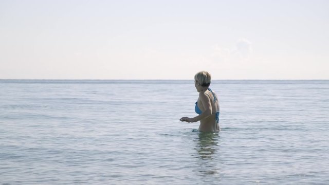 woman in bikini enters cold water of sea experiencing fear.