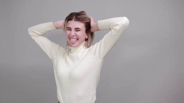 Attractive young pretty woman wearing nice shirt and funny with nice haircut,looking happy and takes hands on head, showing tongue over isolated gray background