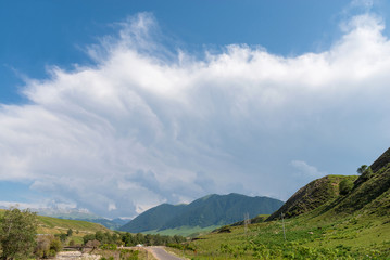 Cloudy sky with green forest mountains and asphalt road