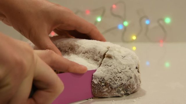 Video Christmas stollen with marzipan being cut with knife. Close up of German Stollen. Selective focus on front of stollen. 4K video preparing stollen. Colorful sparkling lights in the background.