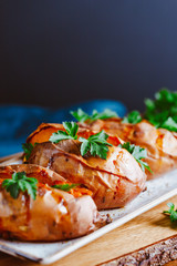 Baked three sweet potatoes with fresh parsley on a white ceramic dish. Healthy veggie dinner or lunch.