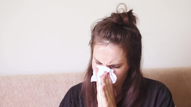 Sick young woman sitting at home with a runny nose.	