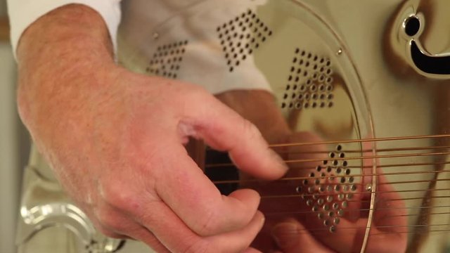 Fingers reflected in a resonator/national steel guitar whilst a man plays. Close up of finger picking hand