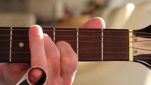 A man plays acoustic slide guitar on a resonator/national steel guitar. Close up of chords/slide hand