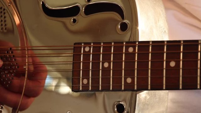 Fingers reflected in a resonator/national steel guitar whilst a man plays. Close up of finger picking hand