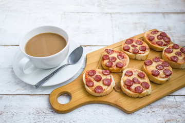 Fototapeta na wymiar homemade mini pizza sandwiches with sausage cheeese round bread on cutting board cup of coffee on white table