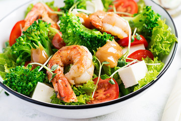 Delicious fresh salad with shrimps / prawns, broccoli, feta cheese, tomatoes, lettuce and peanut dressing. Diet menu. Top view