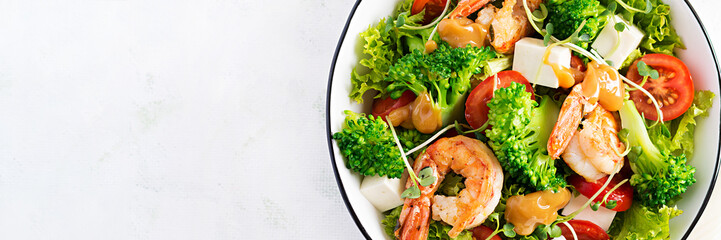 Delicious fresh salad with shrimps / prawns, broccoli, feta cheese, tomatoes, lettuce and peanut dressing. Diet menu. Top view, banner