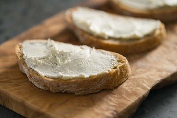 Closeup of three ciabatta slices with cream cheese on olive wood board on terrazzo surface