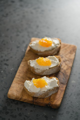 Three ciabatta slices with ricotta and orange marmalade on olive wood board on terrazzo surface