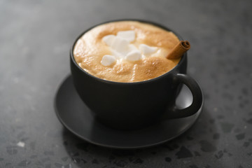 cappuccino with marshmallow and cinnamon in black cup on terrazzo surface