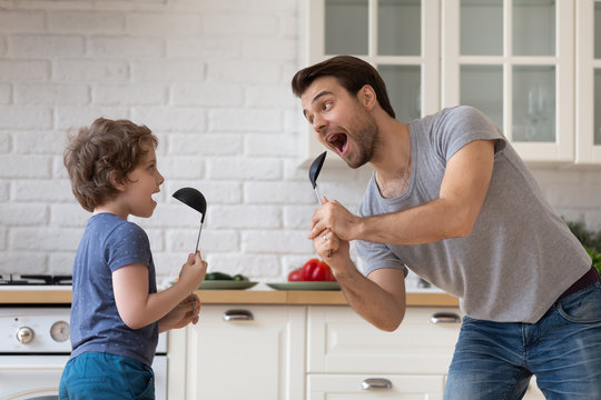 Father dancing with son holding kitchen spoon like microphone singing
